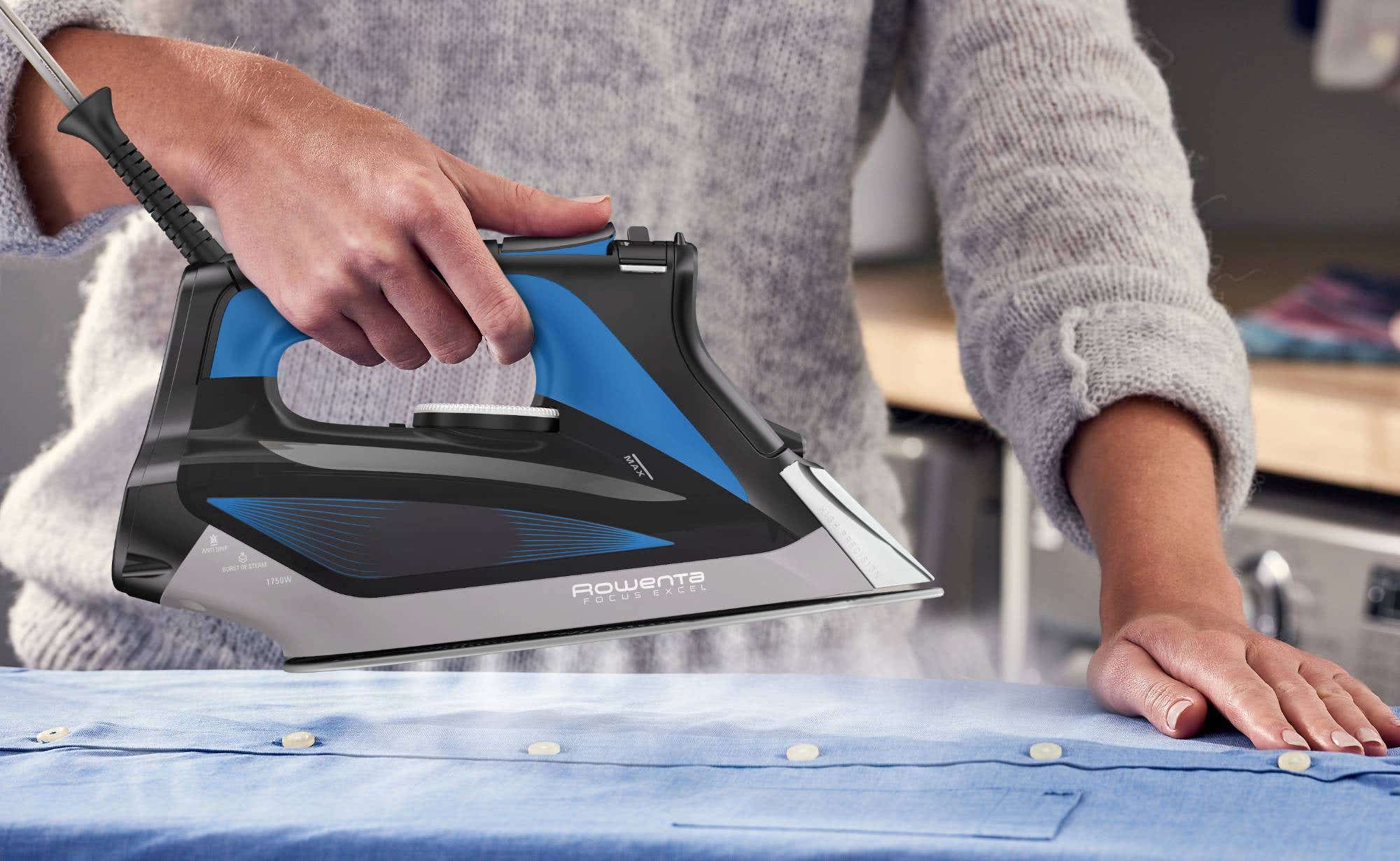 A person operates a blue and black iron, carefully pressing it against a garment to remove wrinkles.