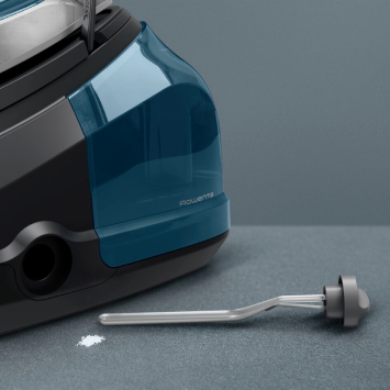 A close-up view of a high-pressure steam generator iron showing the anti-scale collector rod removed from the base, with visible limescale residue next to it.