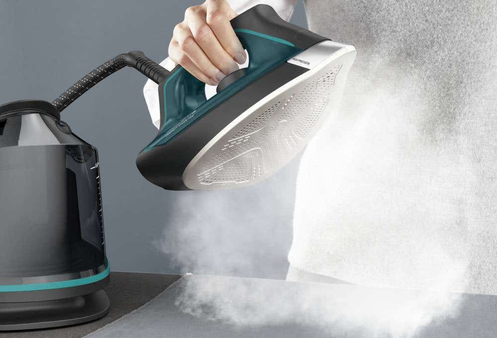 Individual using an iron to apply steam to a surface, effectively smoothing out wrinkles in fabric.